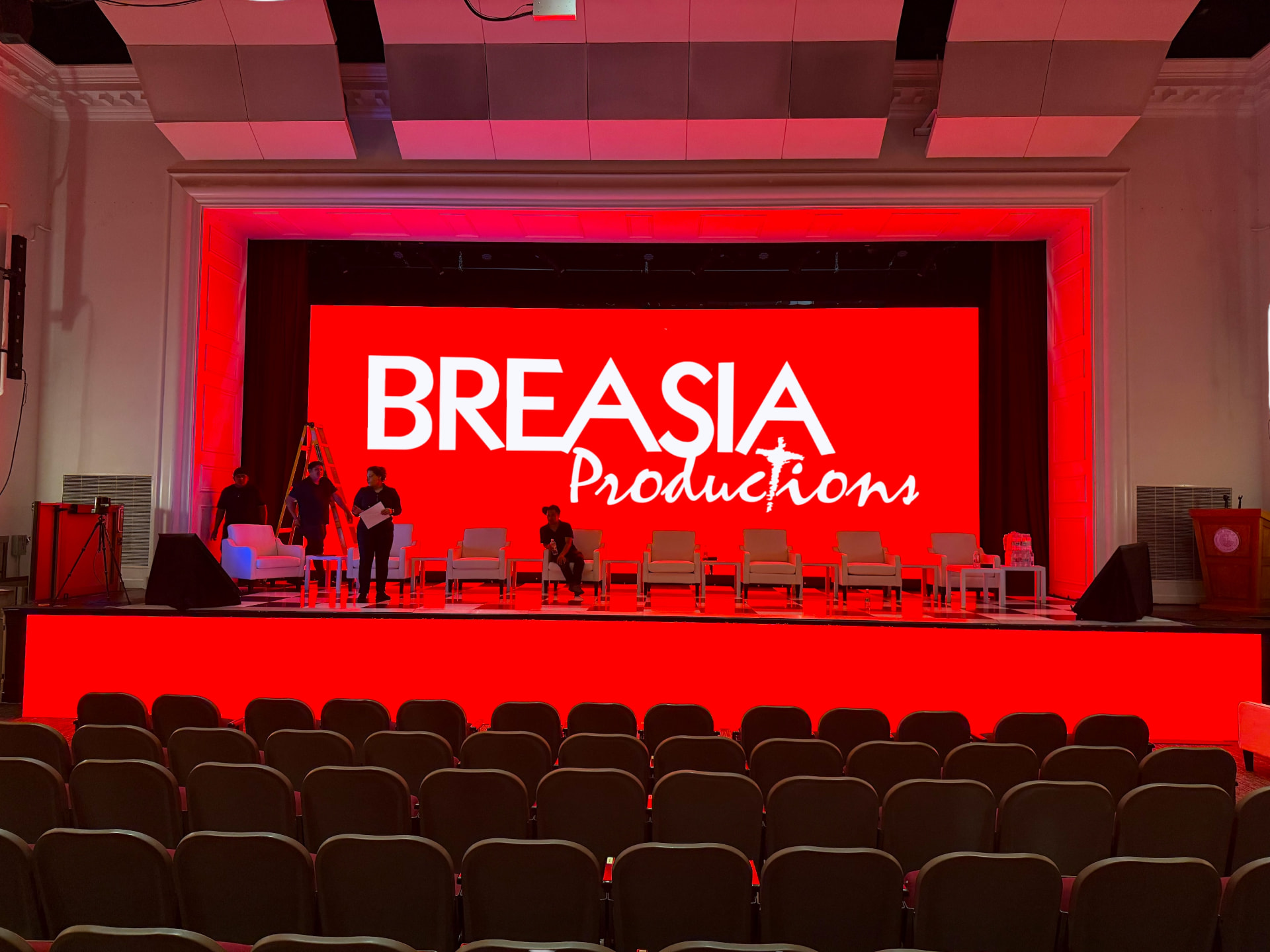 Large LED wall showing the Breasia Productions logo on a theater stage set for a panel